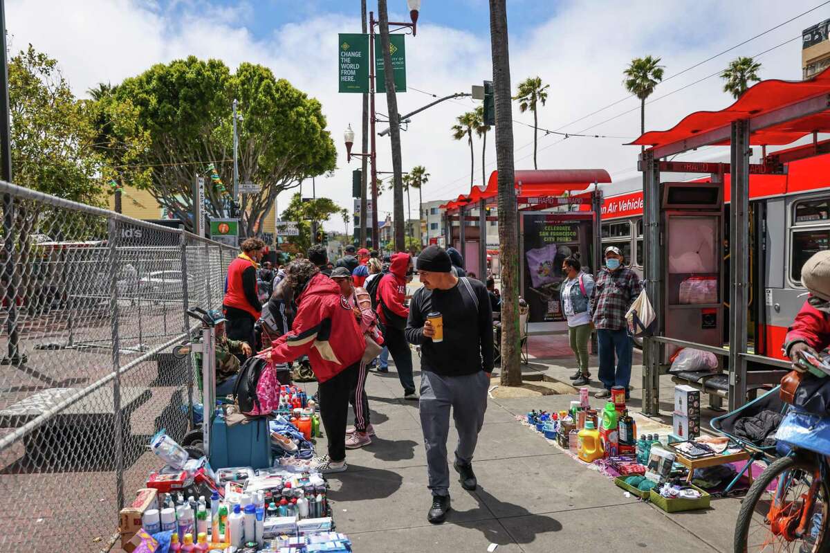 Vendors sell items at the 24th Street BART as people walk by in San Francisco, Calif.,on Thursday, July 21, 2022. A fence was erected around the station in an effort to deter illegal vending and open air drug use