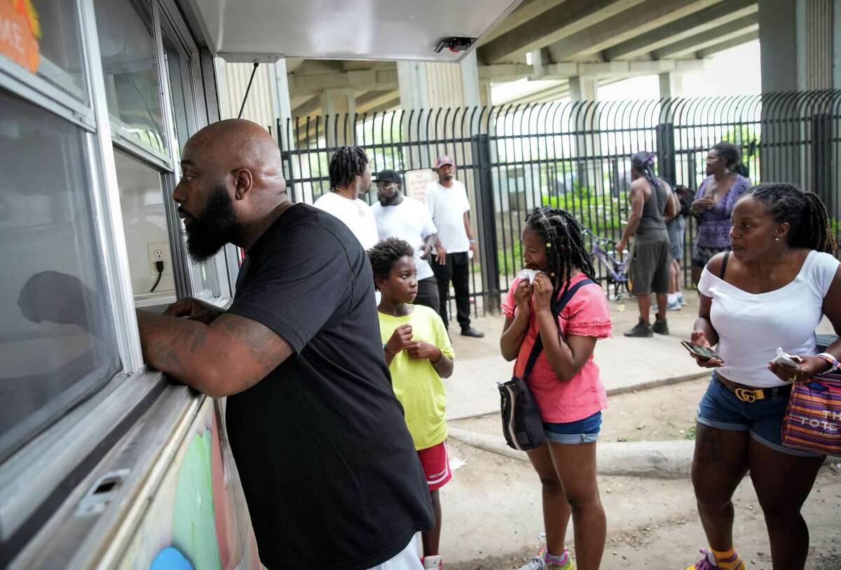 Rapper and community activist Trae Tha Truth, from left, asks for popsicles to hand out as Marvelous Atlee, 12, his sister Lani Dailey, 11, and their mom Shavonne Leon eat popsicles Friday, July 22, 2022, near Minute Maid Park in Houston. The giveaway was organized as part of Trae Day, a celebration and philanthropic event. Trae and volunteers distributed ice cream to people living under I-69. “I’m a huge fan of Trae Tha Truth…he’s a great, positive role model, especially for my son,” Leon said. “This is a great experience,” she said as she talked about how it was good to introduce her son to those who are less fortunate.