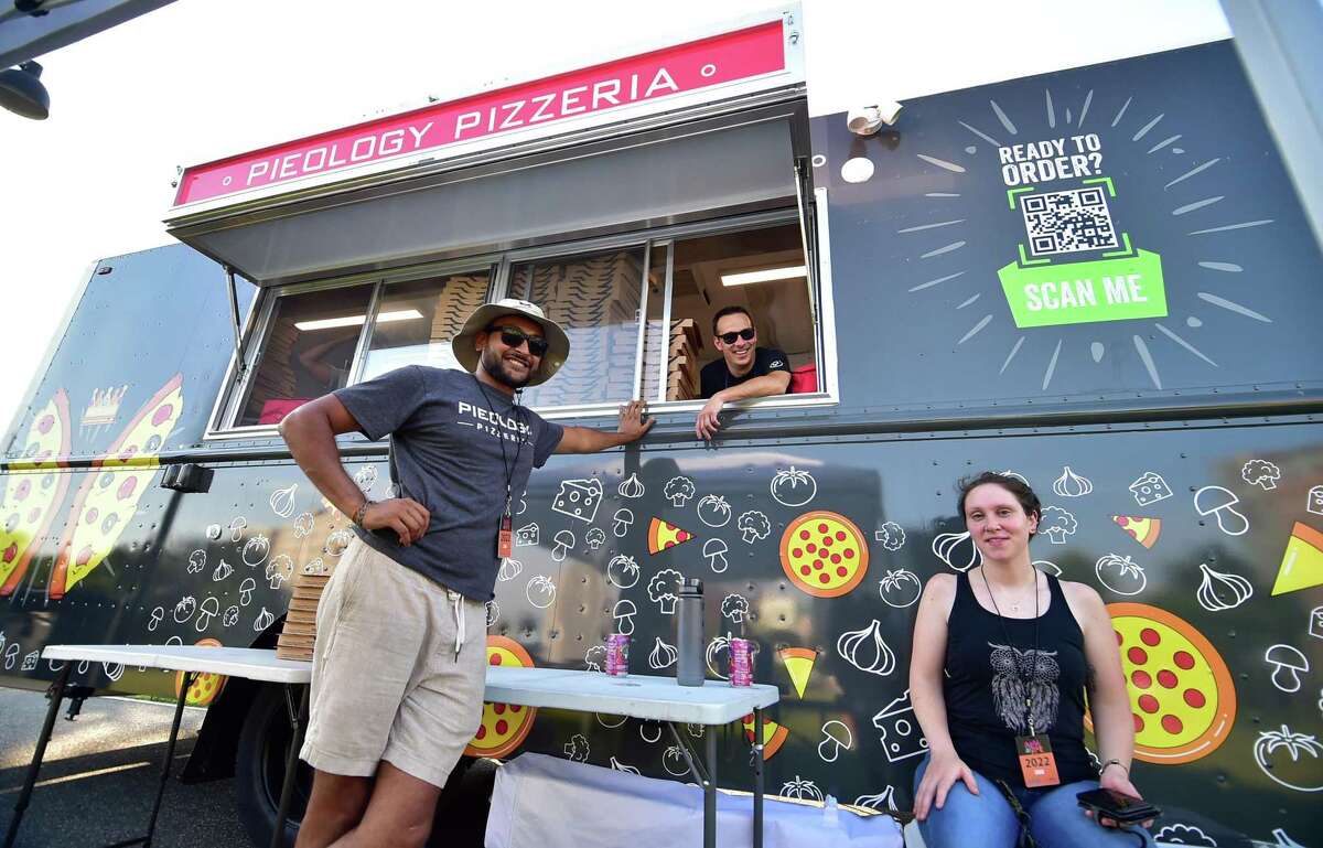 Pieology's Sahil Patel, left, Dennis Frasene, in window and friend Megan McDonald pose in front of the pizza company's food truck during the Alive at Five concert series at Mill River Park in Stamford, Conn., on Thursday July 21, 2022. Pieology Pizzerias are located in Stamford and Brookfield. This is the debut of the Pieology food truck at the Alive at Five concert. The food truck offers up custom-made fresh pizza to Connecticut and New York outdoor festivals, concerts, public events, private parties, corporate parks, beaches and more.