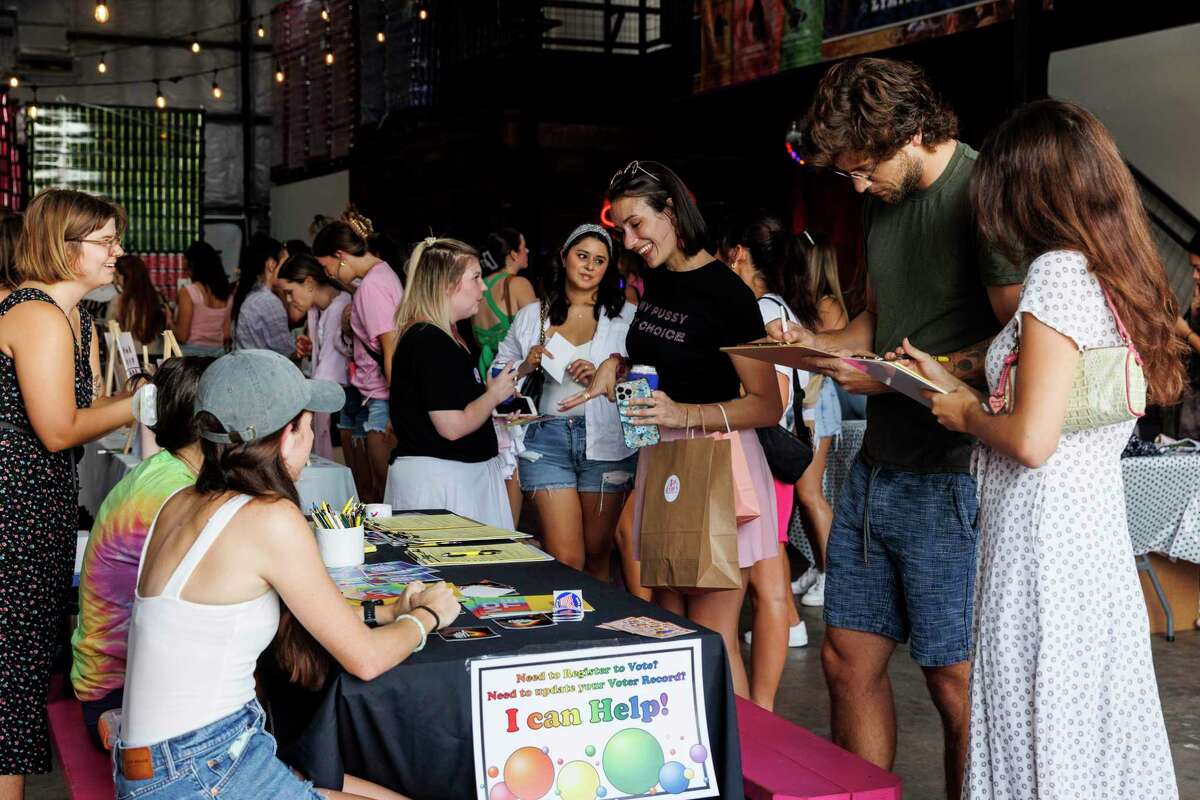 People visit the voter registration table during the Fun(damental Rights) on Weekdays Happy Hour at Blue Norther Hard Seltzer in Austin, Texas, Tuesday, July 12, 2022. The table was crowded with people registering to vote through out the entire happy hour.