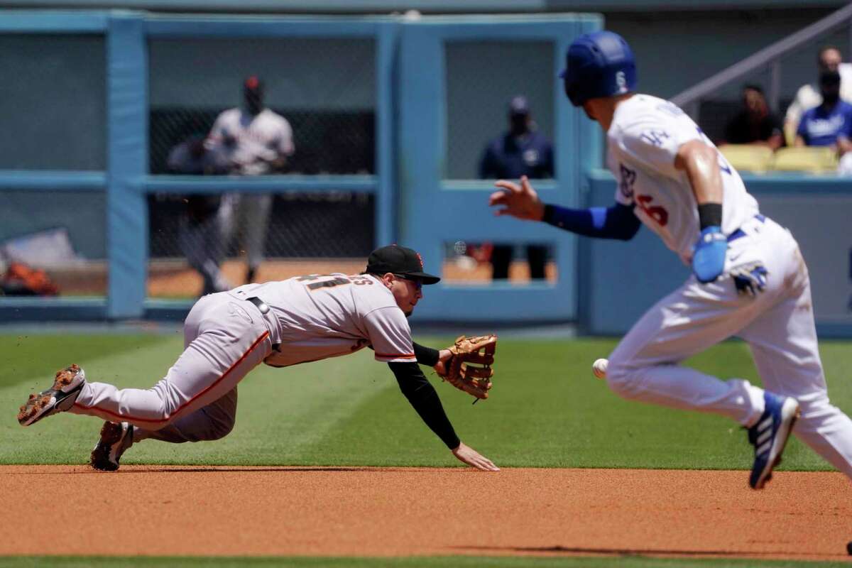 San Francisco Giants second baseman Wilmer Flores, left, can't get a ball hit for an RBI single by Los Angeles Dodgers' Freddie Freeman as Trea Turner, right, runs to second during the first inning of a baseball game Sunday, July 24, 2022, in Los Angeles. (AP Photo/Mark J. Terrill)