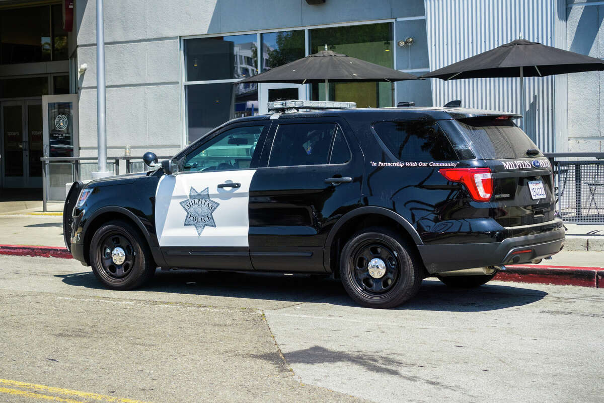 A Milpitas police car stopped on the side of the road in front of a restaurant.