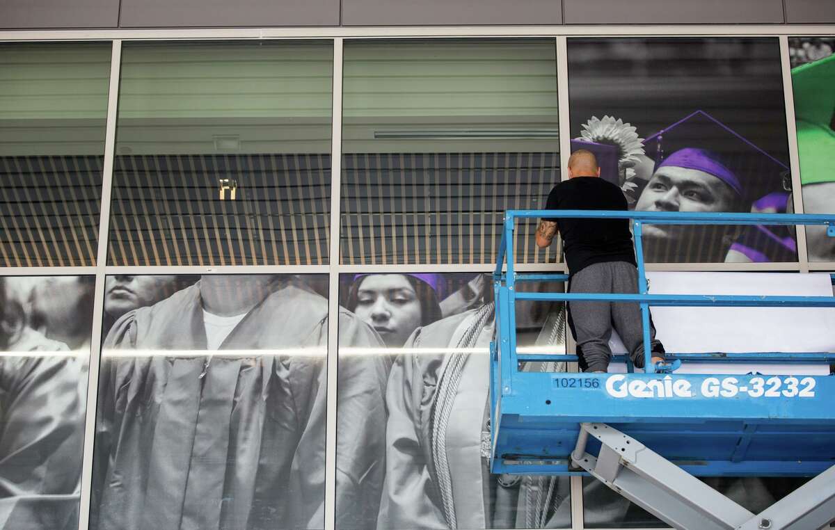 A worker puts up posters on windows of the Alamo College District building support offices for its opening in 2019.
