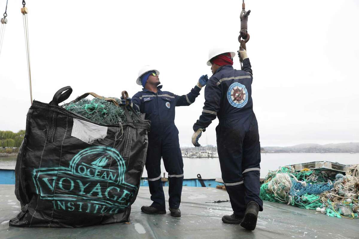 Deckhand Iakoba Kirario (left) and abled seaman Ieie Teibitoa move a large bag of plastic junk collected from the “Great Pacific Garbage Patch” on a Pacific clean-up voyage by Ocean Voyages Institute.