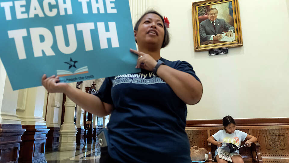 Houston ISD teacher, Maria Benzon, holds up a Teach the Truth poster as her daughter an HISD student, Edita-Sage Bitner, 7, reads a book on the bench behind her on Tuesday, July 26, 2022, in Austin, Texas. Benzon and other attendees read from some of the books being targeted for banning during a Texas Freedom Network’s Teach the Truth Coalition read-in demonstration held at the Texas State Capitol Rotunda.