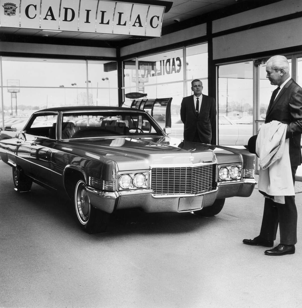 A man looks at a new Cadillac sedan in a showroom, as a car salesman looks on, early 1970s. (Photo by Hulton Archive/Getty Images)