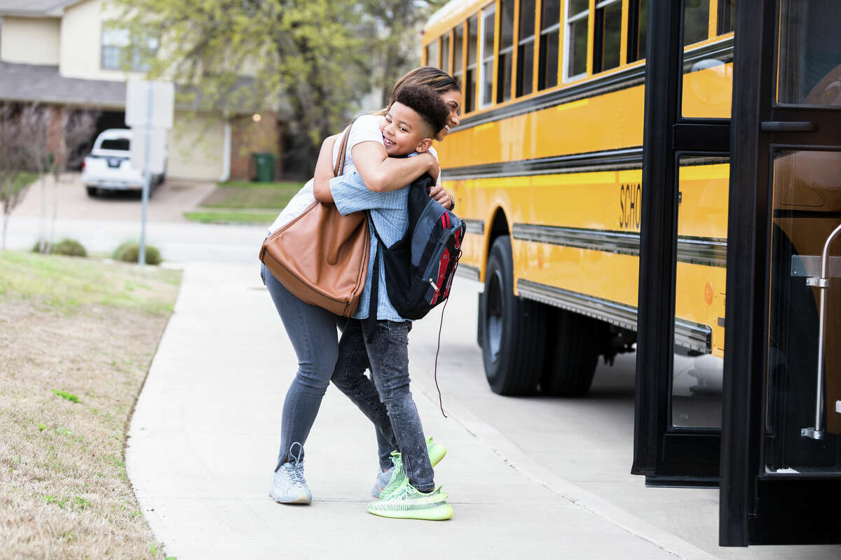 A caring mid adult mom gives her son a big hug as he gets of school bus in his neighborhood.