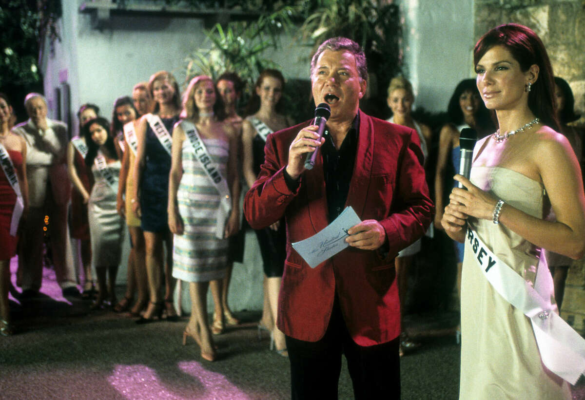 William Shatner speaks into a microphone next to Sandra Bullock in a scene from the film 'Miss Congeniality', 2000.