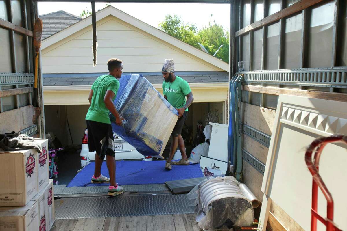 David Stoglin, left, and Jonathan Nieves carry a piece of furniture into the back of a Bellhop truck while packing and loading up a household for a move Thursday, July 28, 2022 in Tomball.