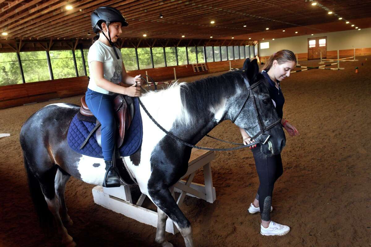 Trainer Sarah Topar walks with student Gemma Porrino, riding a horse name Jeffy, during a riding lesson in the indoor arena at Salko Farm & Stable, in Fairfield, Conn. July 27, 2022.