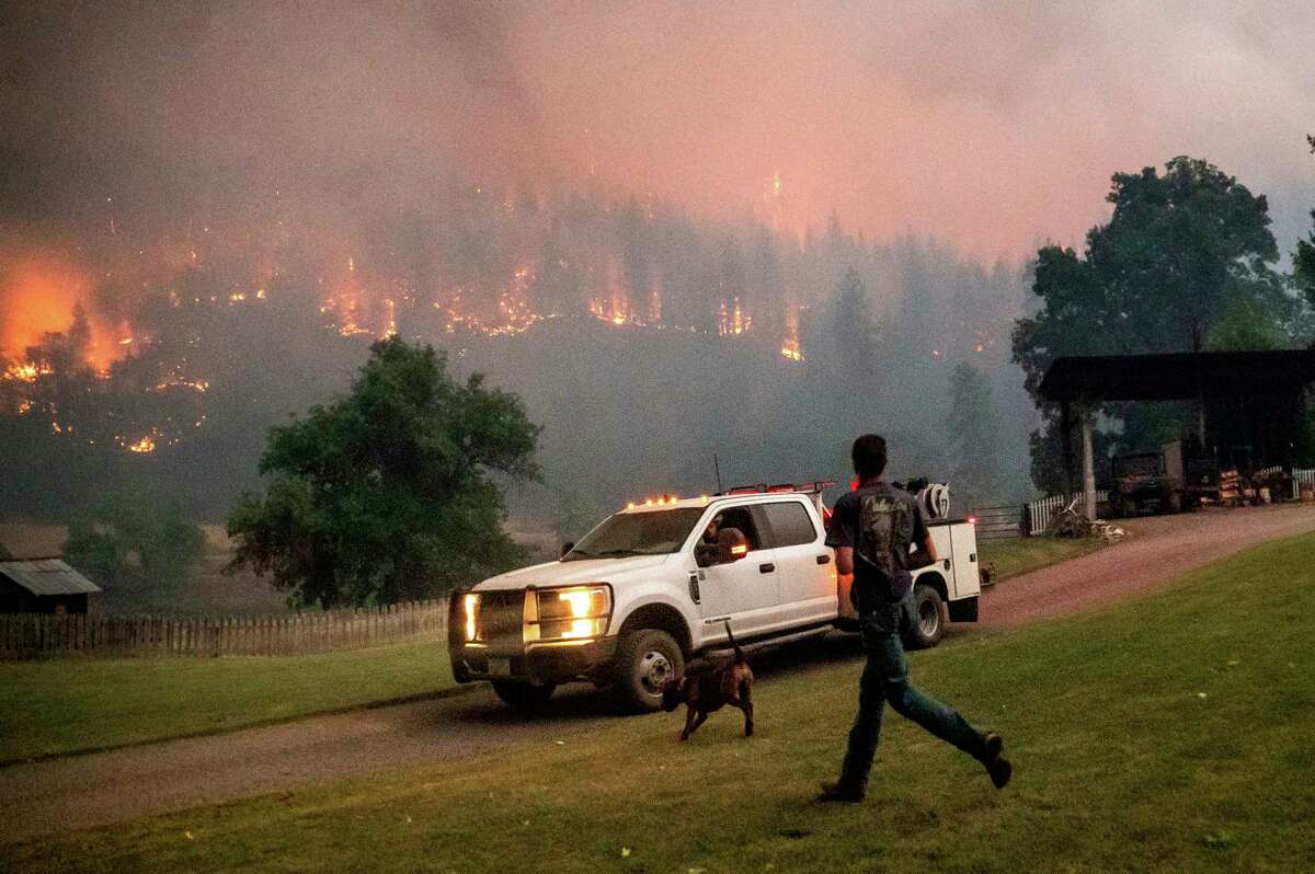 Een man rent naar een vrachtwagen terwijl een bosbrand genaamd de McKinney-brand op zaterdag 30 juli 2022 in Klamath National Forest, Californië, brandt.