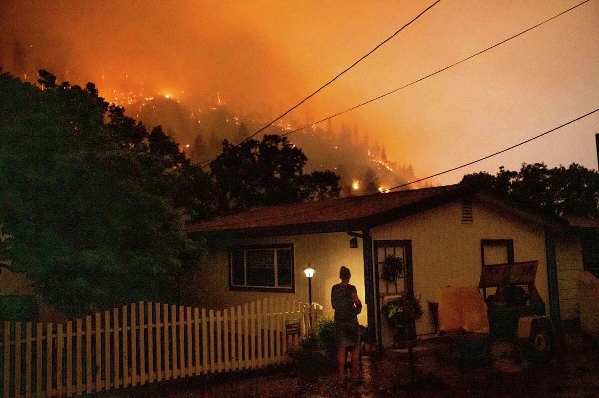 Angela Crawford walks past her home as a wildfire called the McKinney fire burns above it in Klamath National Forest, Calif., on Saturday, July 30, 2022. Crawford and her husband stayed, as other residents evacuated, to defend their home from the fire.