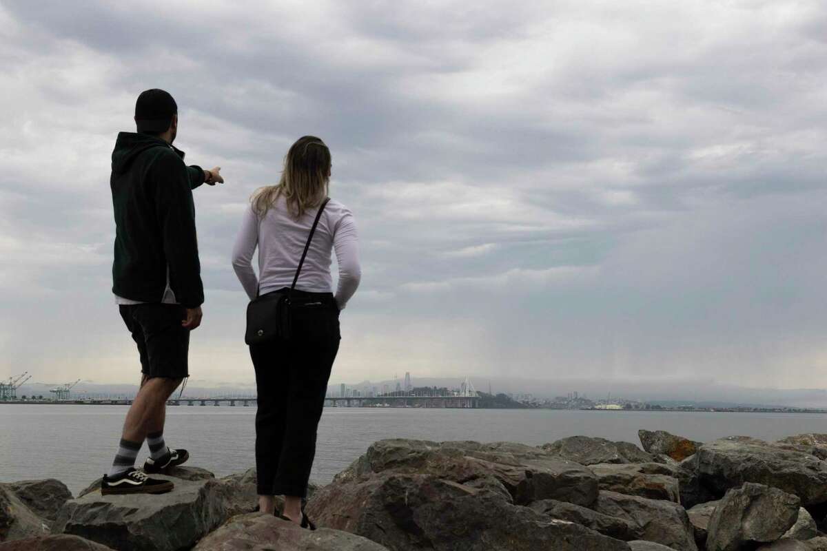 2022年8月1日，星期一，加利福尼亚州埃默里维尔，一名男子站在埃默里维尔码头的大片乌云下，指着旧金山。