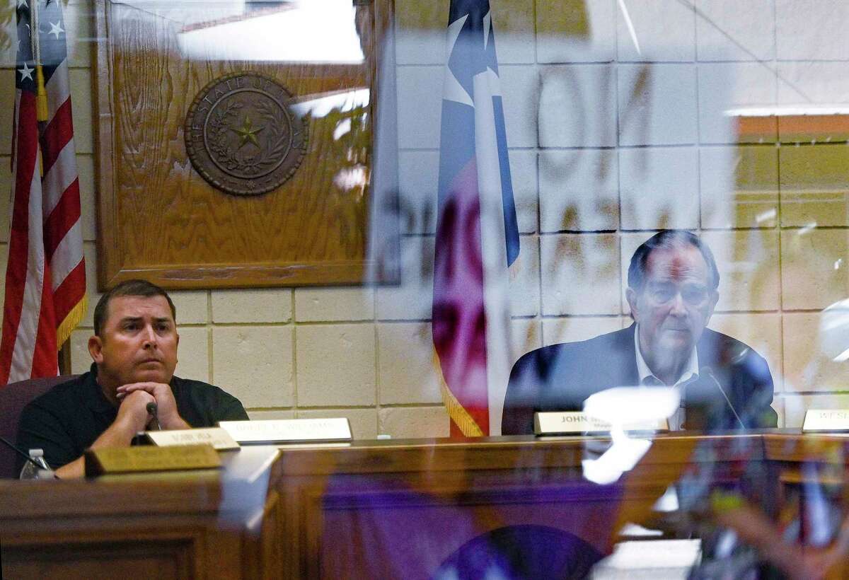 Mayor John McAnelly, right, and councilman Brett Williams listen to a speaker as a protester’s sign reading “No weapons of war” is reflected in a window at Monday’s Hondo City Council meeting. The council rescinded an agreement to rent city property for a planned National Rifle Association event that would have included a raffle of an assault rifle.