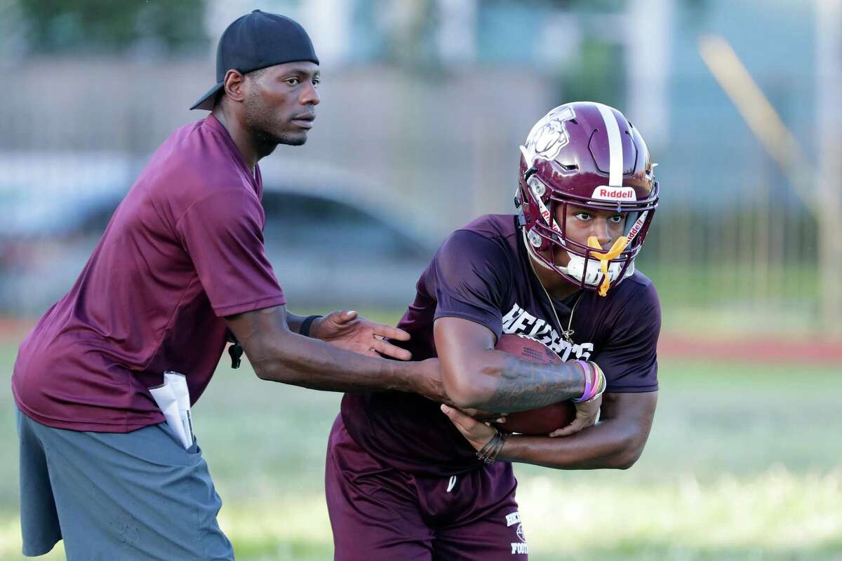 Assistant coach Freddie Stoglin, left, hands off to running back Braiden Wooley, right, during a no-pads football practice at Heights High School Tuesday, Aug. 2, 2022 in Houston, TX.