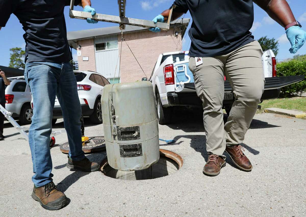 Houston Health Dept., employees Muhammad Farhad, left, and Kendra Davis remove a sampler from a sewer line as they prepare to collect water samples on Wednesday, July 20, 2022 in Houston. 