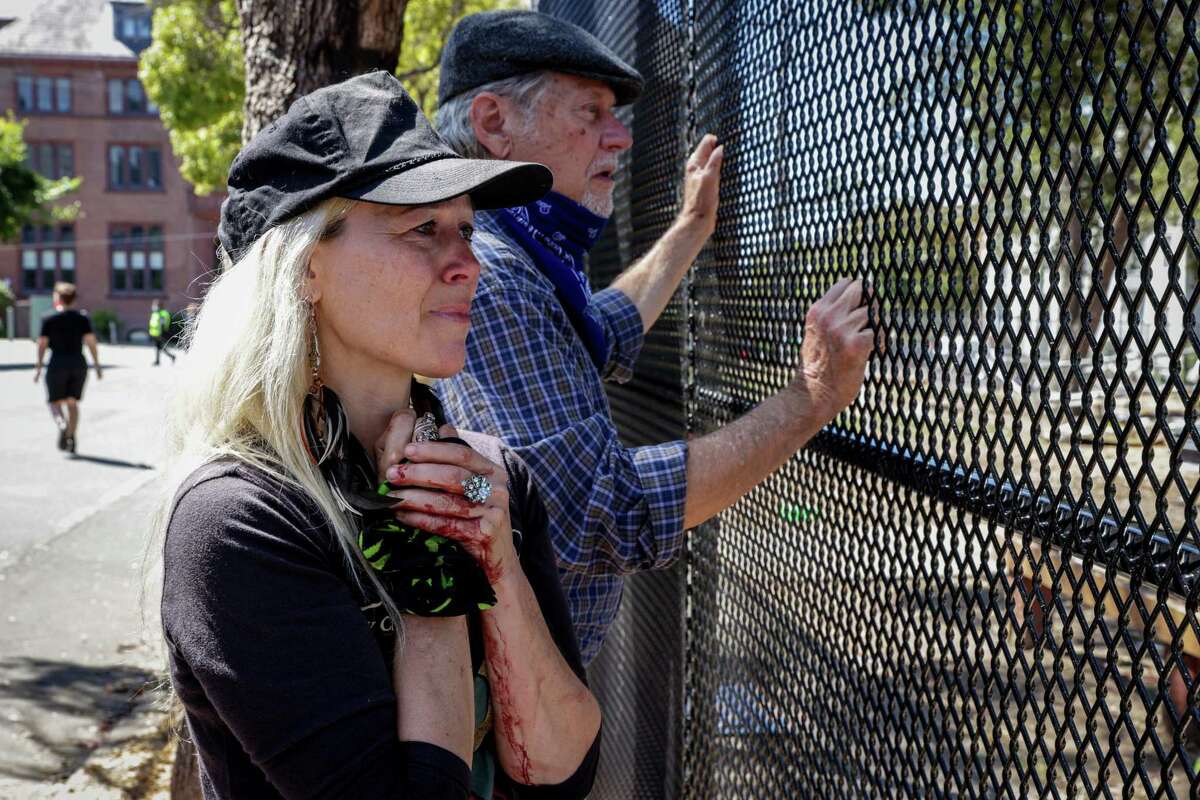 Naya Rose clutches her bleeding hands as she watches construction at People's Park in Berkeley, Calif., on Wednesday, Aug. 3, 2022. Rose said the gate that closes the park to protesters severed her hand.  Those against construction in the park gathered by the dozens to denounce the cleanup of the park in preparation for the development of student housing.