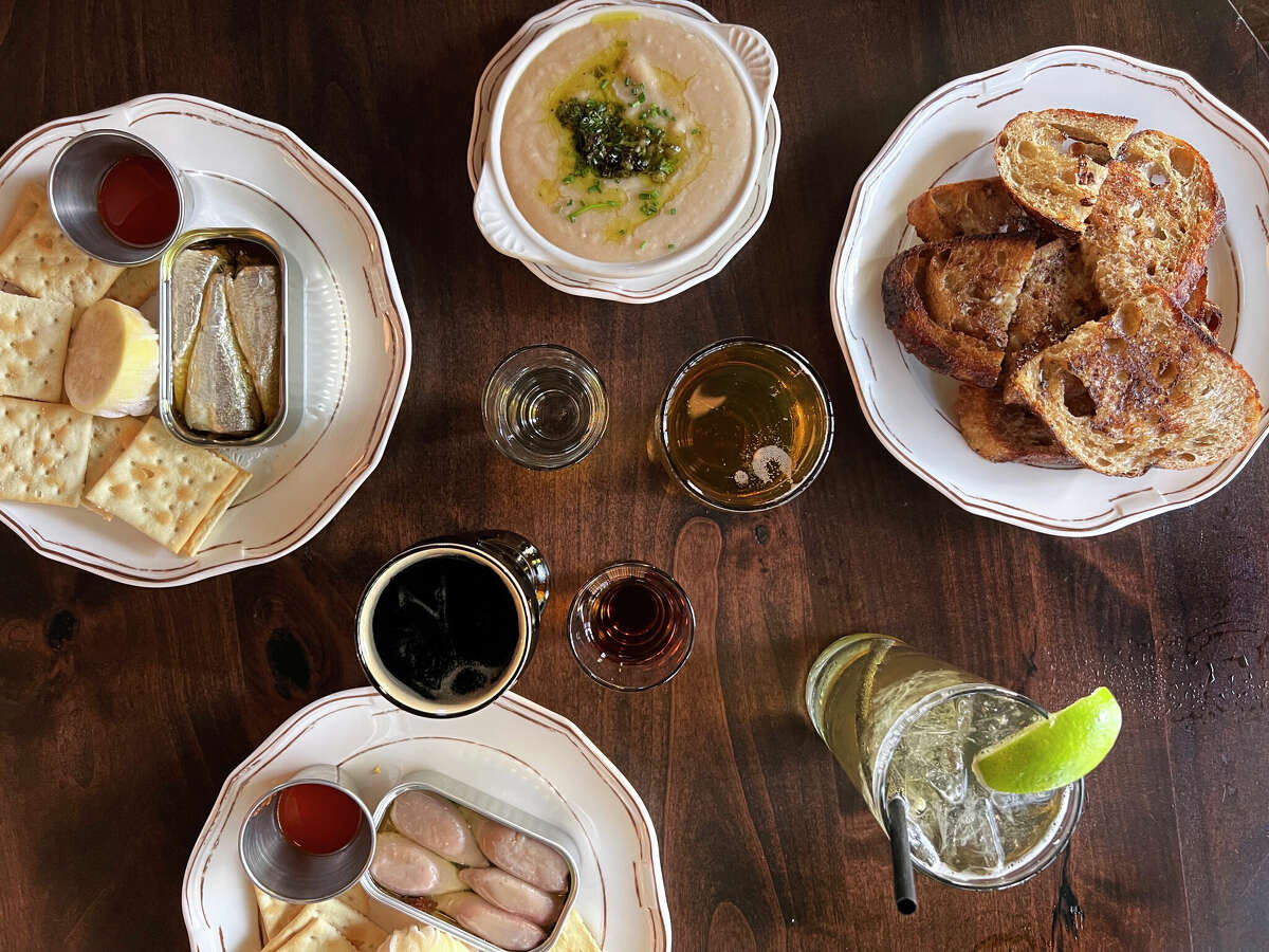 Food and drinks at Double Standard, a tavern and restaurant at the Rand Building in downtown San Antonio, include, clockwise from left, tinned sardines, mezcal, Modelo beer, white bean dip and toast, a whiskey-and-soda, amaro liqueur, (512) Pecan Porter and stuffed squid conservas. 