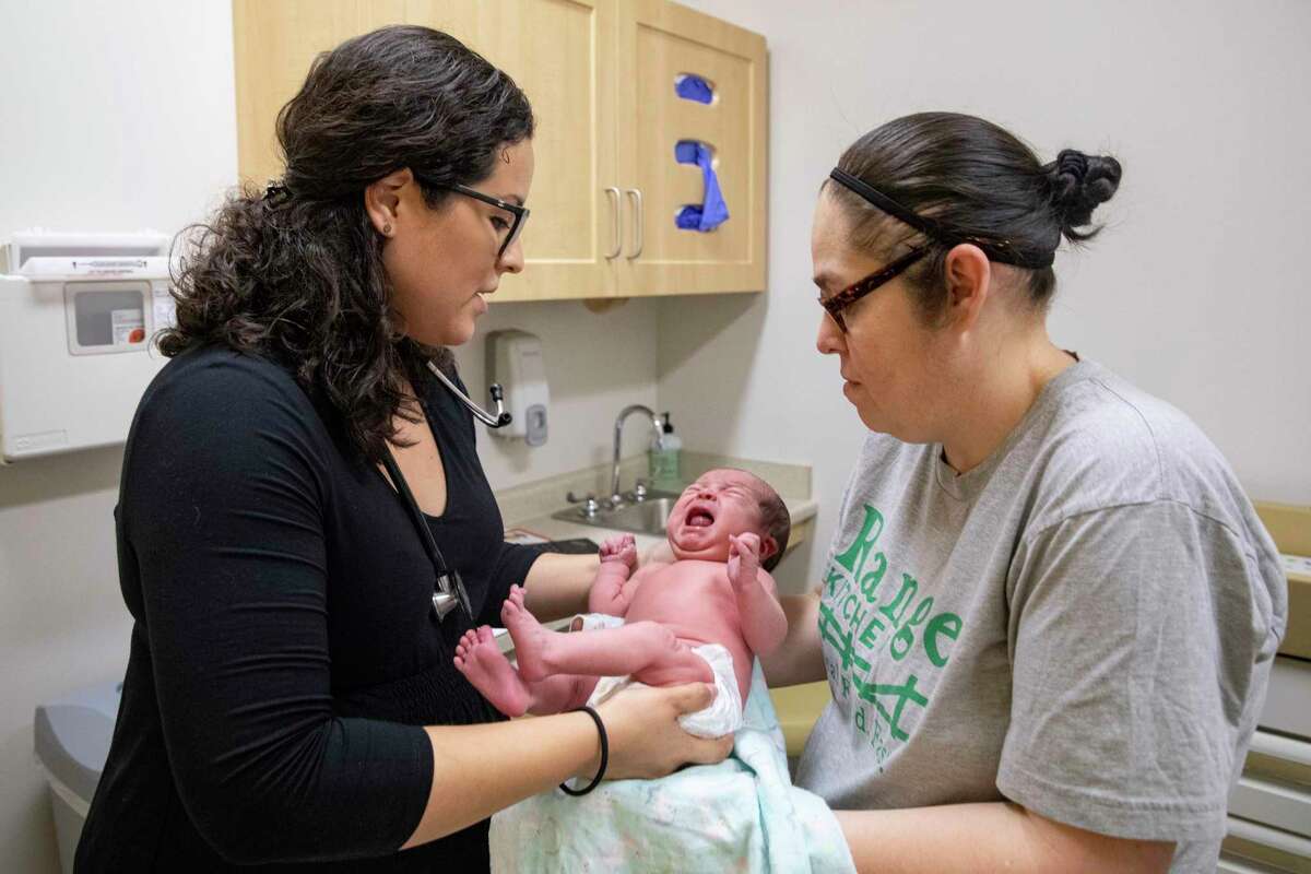 Dr. Jasmine Saavedra, left, a pediatrician at Esperanza Health Centers in Chicago, hands newborn Alondra Marquez to her mother, Esthela Nuñez, right, after examination.