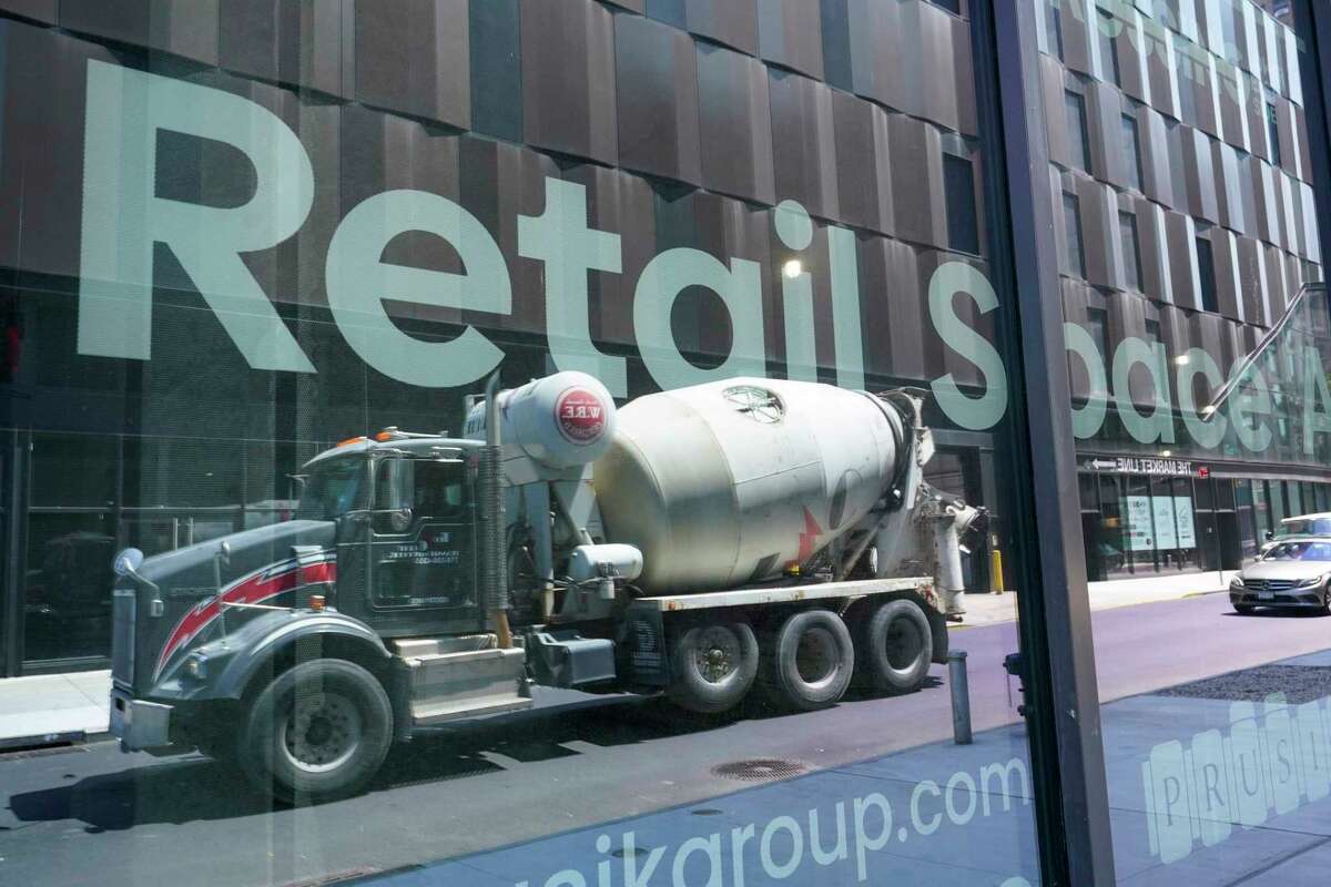 A cement mixer truck is reflected on a window of window advertising retail space for rent at a residential and commercial building under construction at the Essex Crossing development on the Lower East Side of Manhattan, Thursday, Aug. 4, 2022. On Friday, Aug. 5, the Labor Department delivers its July jobs report.