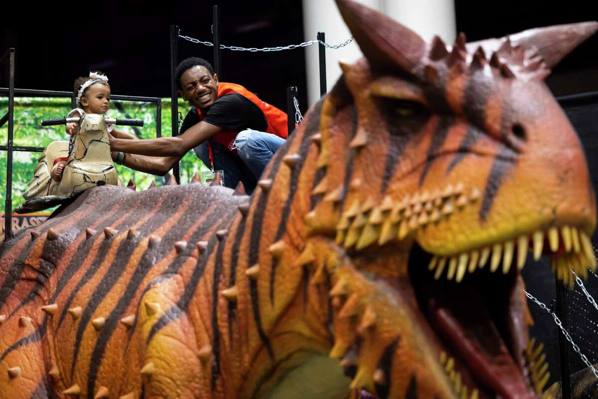 Aurtrel Black gives 1-year-old Juliana Newkirk a hand on top of one of the dinosaurs at the Jurassic Quest exhibit at NRG on Thursday, Aug. 4, 2022.