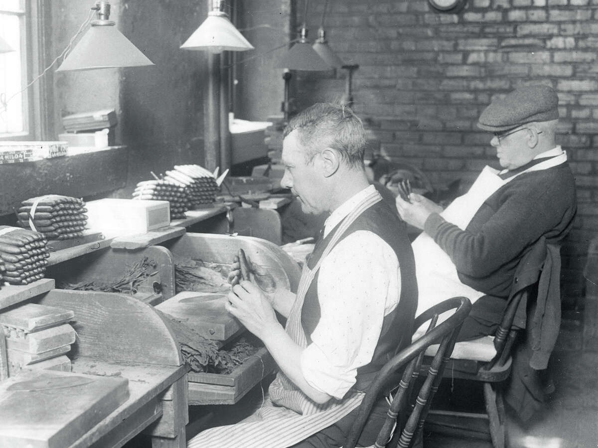 Two men roll cigars, the last step of the cigar-making process.