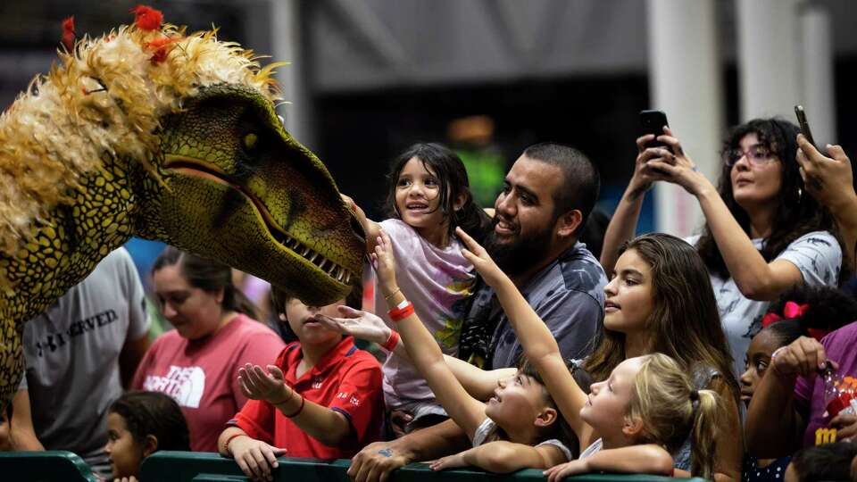 Attendees pet a walking raptor at the Jurassic Quest exhibit at NRG on Thursday, Aug. 4, 2022.