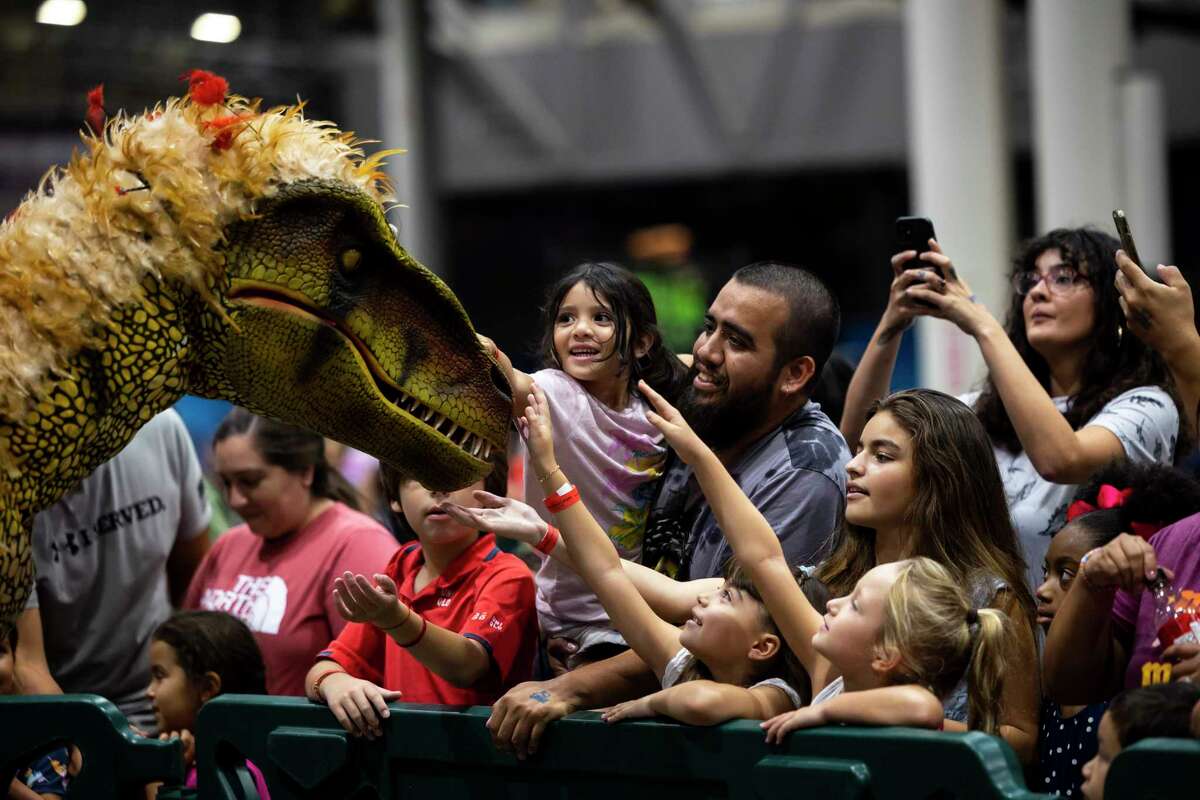 Attendees pet a walking raptor at the Jurassic Quest exhibit at NRG on Thursday, Aug. 4, 2022.