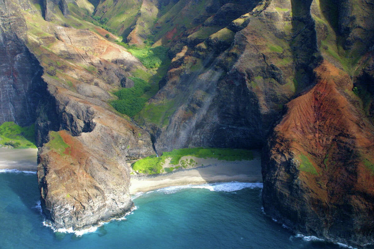 An aerial of Honopu Beach and its valley hanging above.  The beach is bisected by a natural arch, often seen in movies.