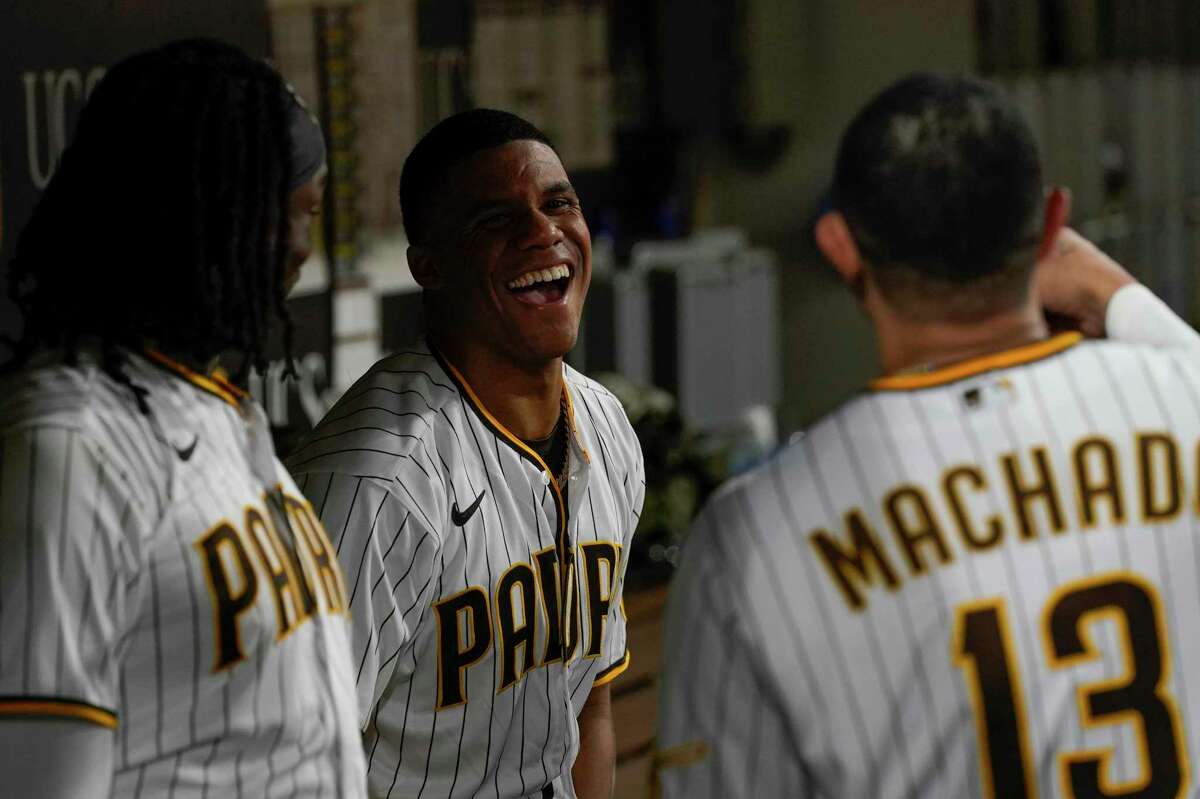 San Diego Padres right fielder Juan Soto, center, jokes with teammates third baseman Manny Machado, right, and first baseman Josh Bell during the fourth inning of a baseball game against the Colorado Rockies, Wednesday, Aug. 3, 2022, in San Diego. (AP Photo/Gregory Bull)