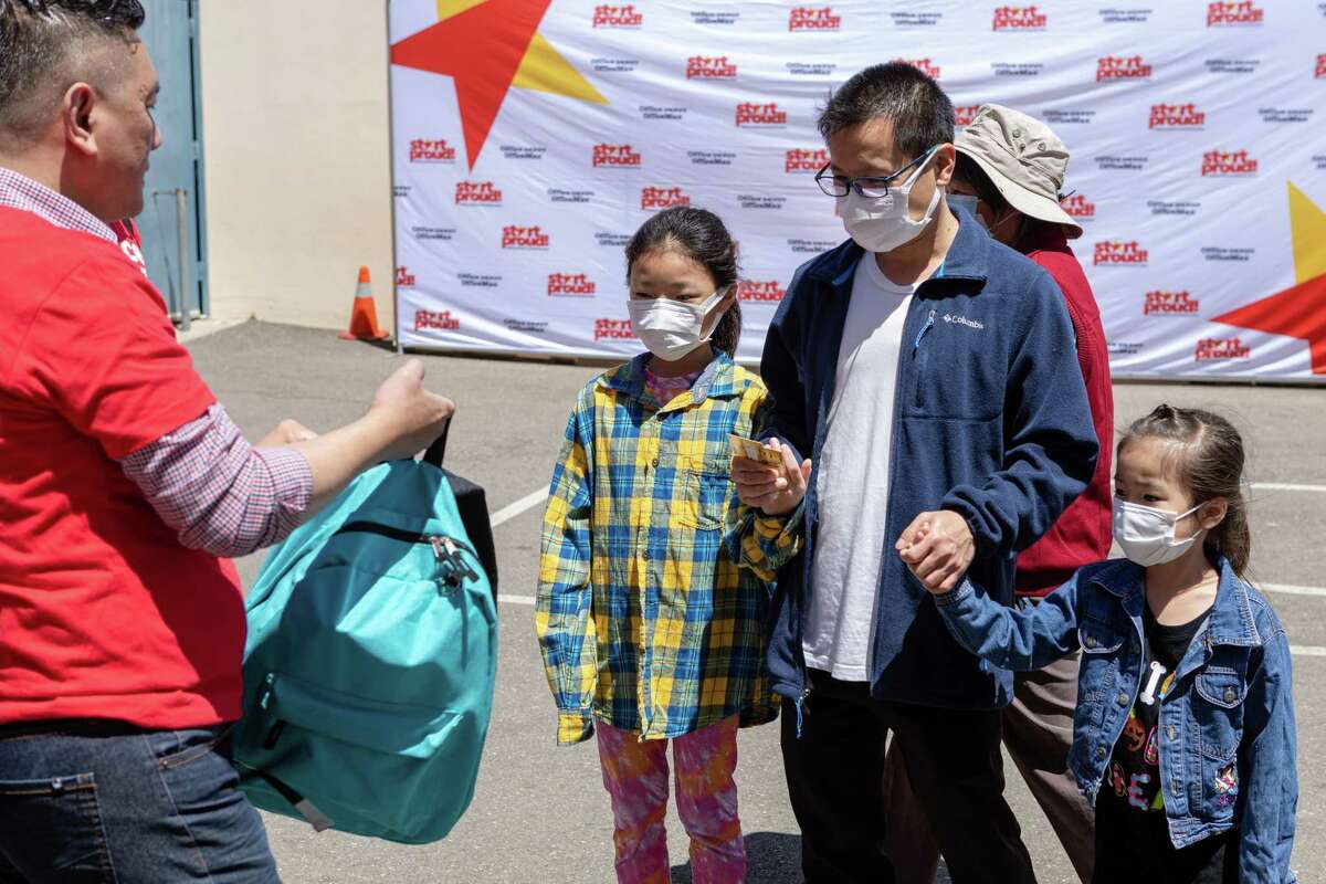 Ben Wu and his daughters Mindy (left) and Michelle receive backpacks from Nhan Nguyen, general manager at Office Depot, at Lincoln Elementary School on Friday, August 5, 2022, in Oakland, Calif.
