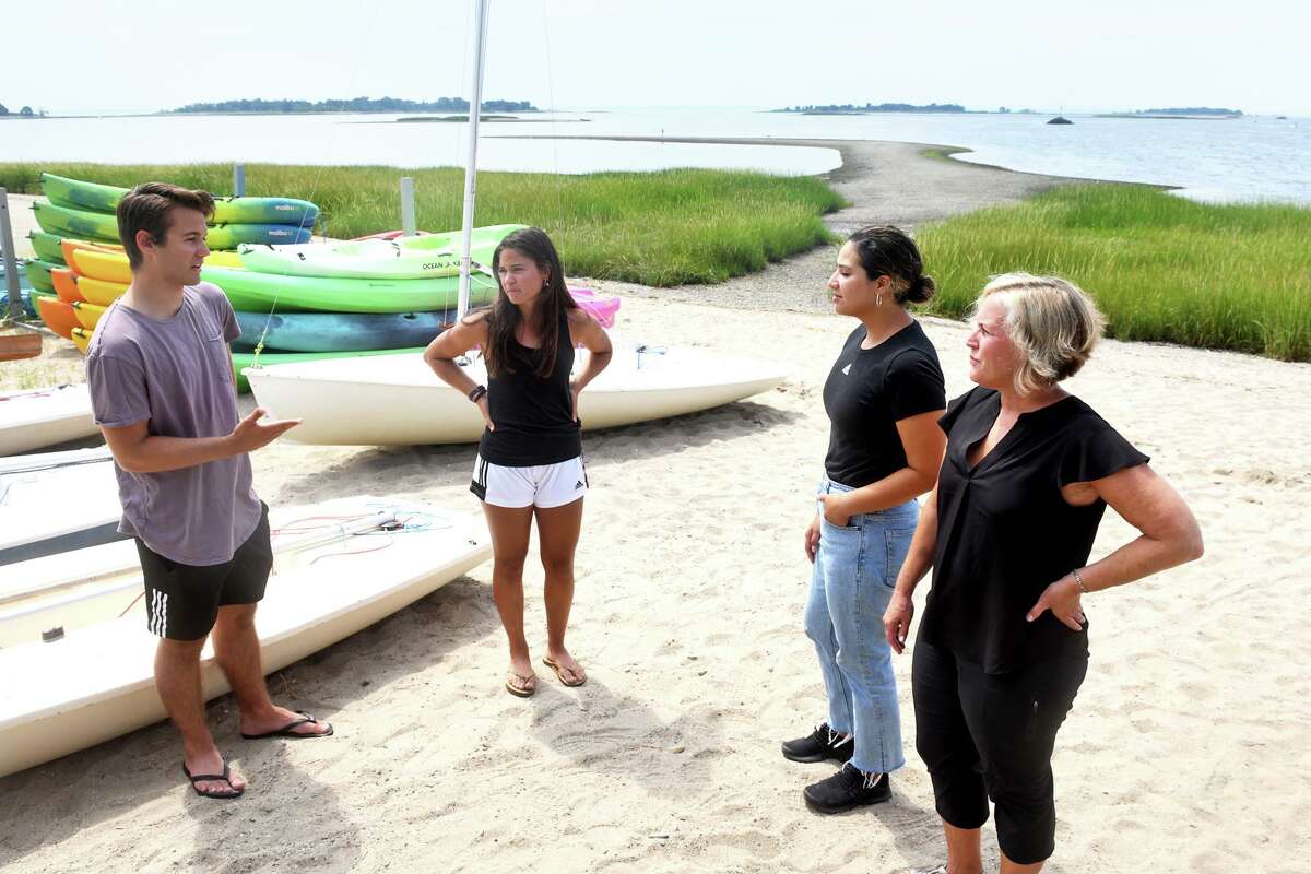From left, Nick Suarez and his sister, Jacqueline, talk with Jennifer Gonzalez and Maya Santangelo at the Norwalk Sailing School, in Norwalk, Conn. Aug. 5, 2022. The four were part of a rescue effort to try and save a man from the waters near a sandbar, seen here in the distance, last Sunday. The man, Mauricio Rodas-Garcia, drowned while trying to save his wife who had fallen into the water.