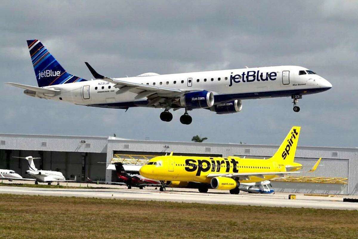 A JetBlue airliner lands past a Spirit Airlines jet on taxi way at Fort Lauderdale Hollywood International Airport on Monday, April 25, 2022. (Joe Cavaretta/Sun Sentinel/TNS)