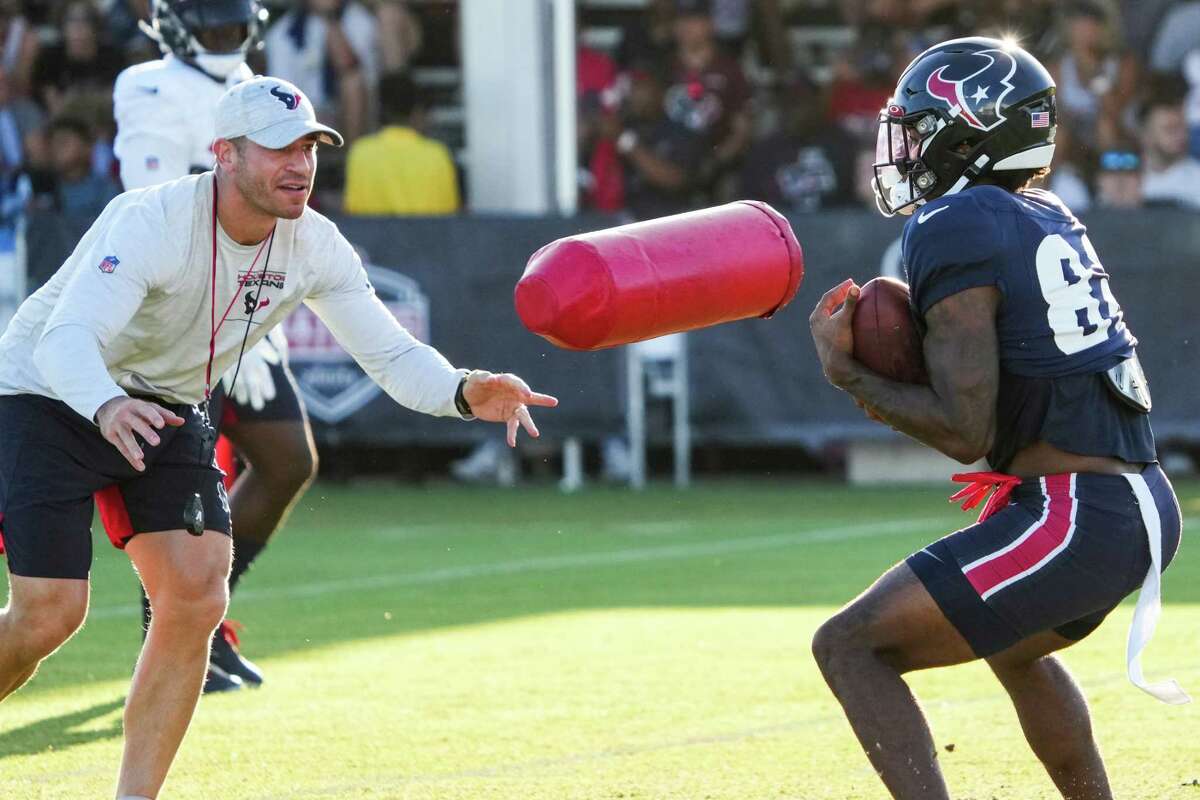 Houston Texans special teams coordinator Frank Ross tosses a blocking pad at wide receiver Connor Wedington (82) as he catches a kick during an NFL training camp Tuesday, Aug. 9, 2022, in Houston.