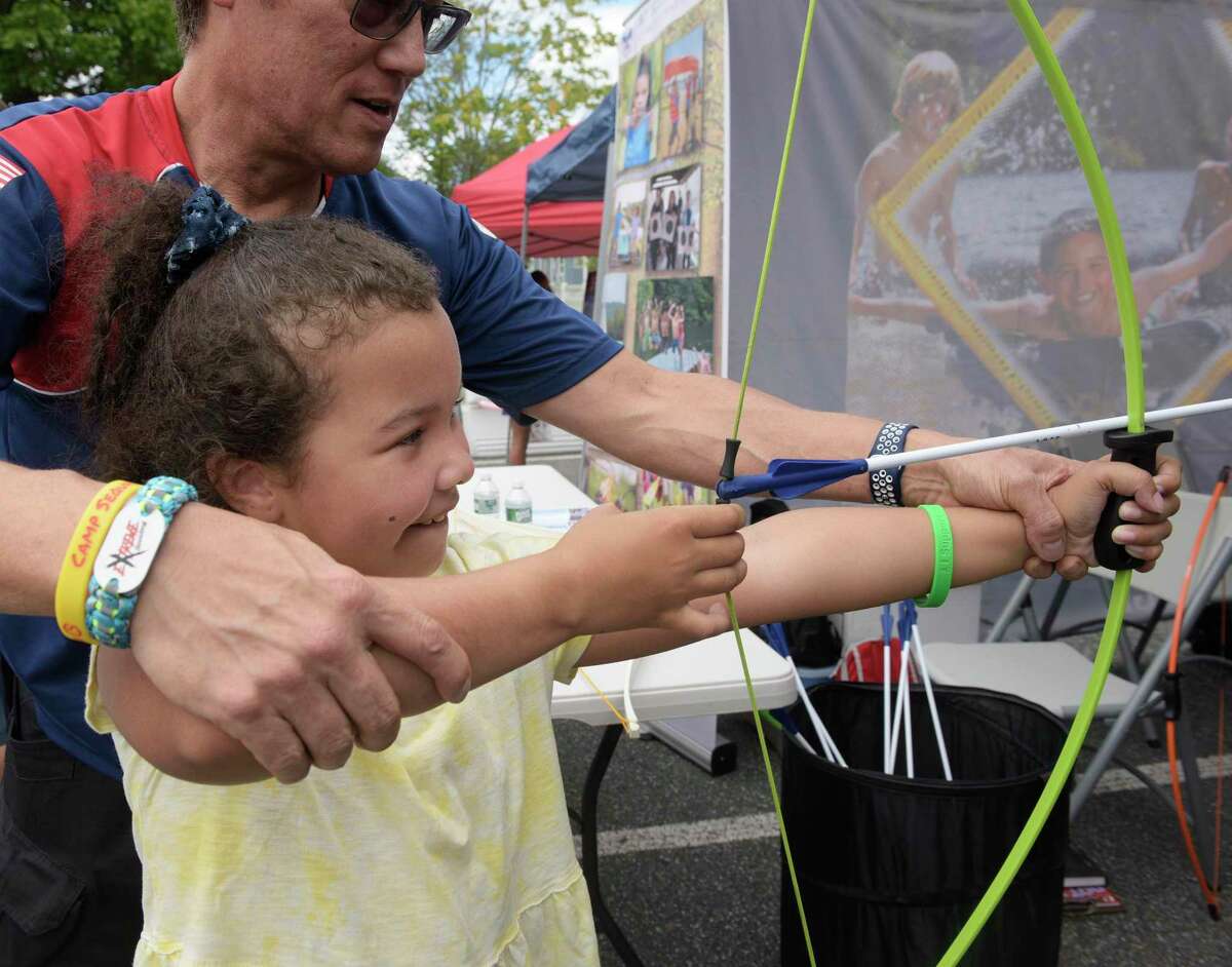 Esther Vieira, age 8, of Danbury, tries out a bow and arrow with the help of Mike Morrell , a scout staffer, at the Boy Scouts of America tent, at the Connecticut Institute for Communities Community Health Fair, part of National Health Center Week. The event will be held in the parking lot of the Danbury Community Center. Wednesday, August 10, 2022, Danbury, Conn.