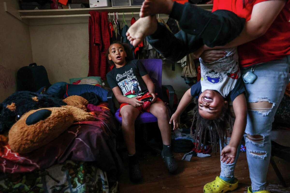 King Tari Johnson, 8 (left), plays video games as sister Celeste Wood, 15, flips brother Kiro Johnson, 3, in their home in Stockton.