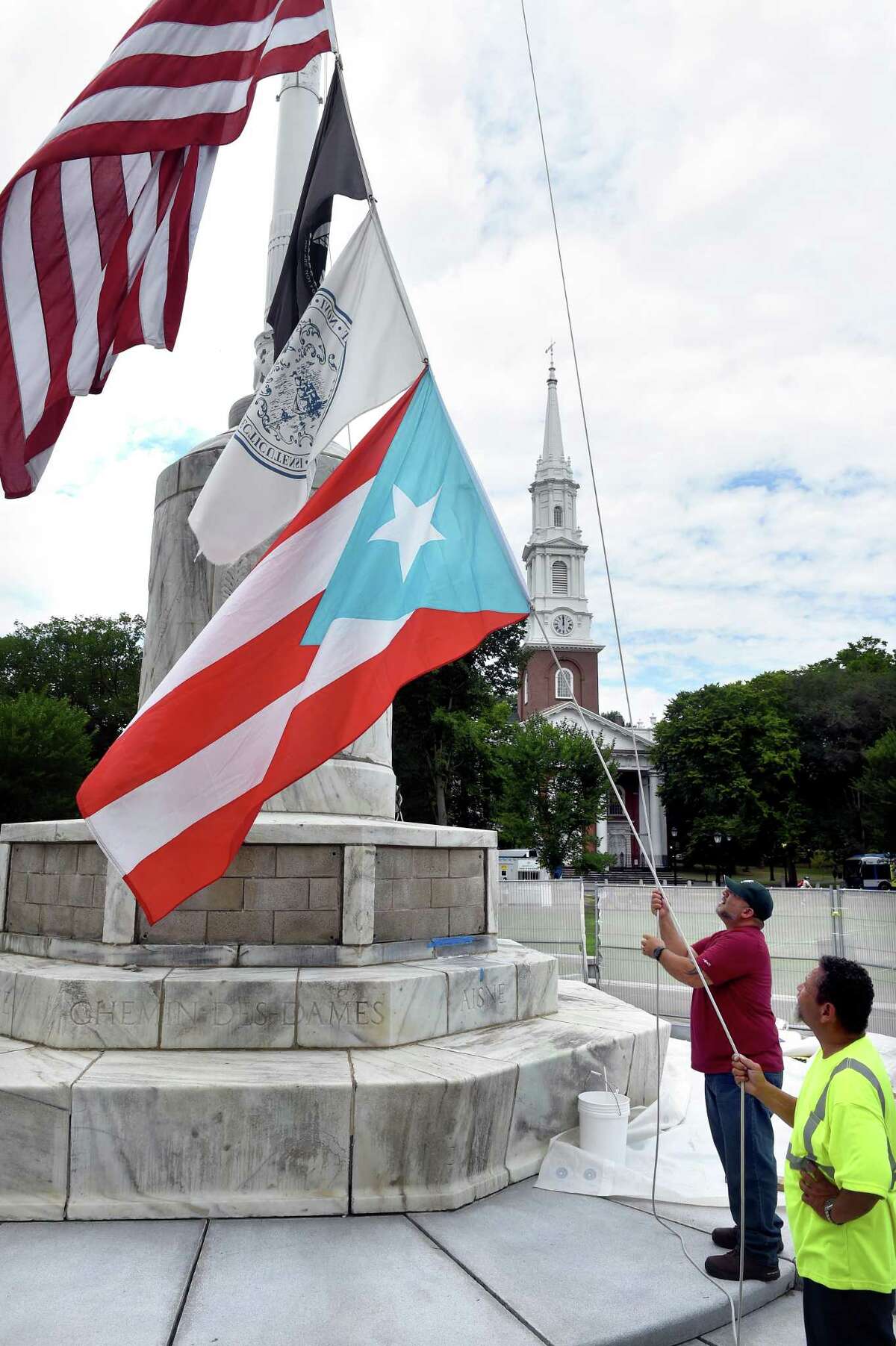 New Haven Department of Parks, Recreation and Trees employees Jose Aviles, left, and Luis Zayas prepare to raise the Puerto Rican flag on the New Haven Green Thursday during a ceremony announcing the 2022 Puerto Rican Festival of New Haven on Saturday.