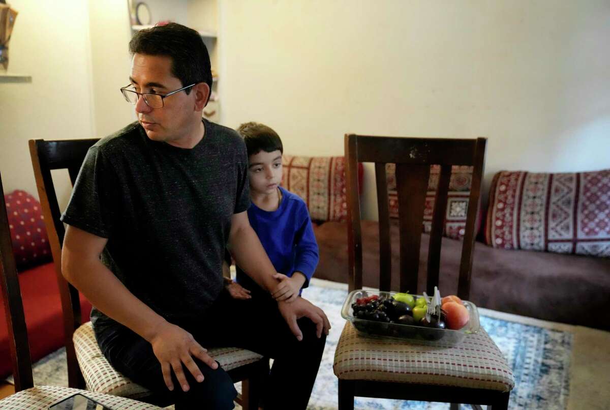 Suliman Jahadullah, 3, clings to his dad, Jahad Jahadullah, who is asking his wife to bring their electric bills while he talks in his apartment, Wednesday, Aug. 3, 2022, in Houston.