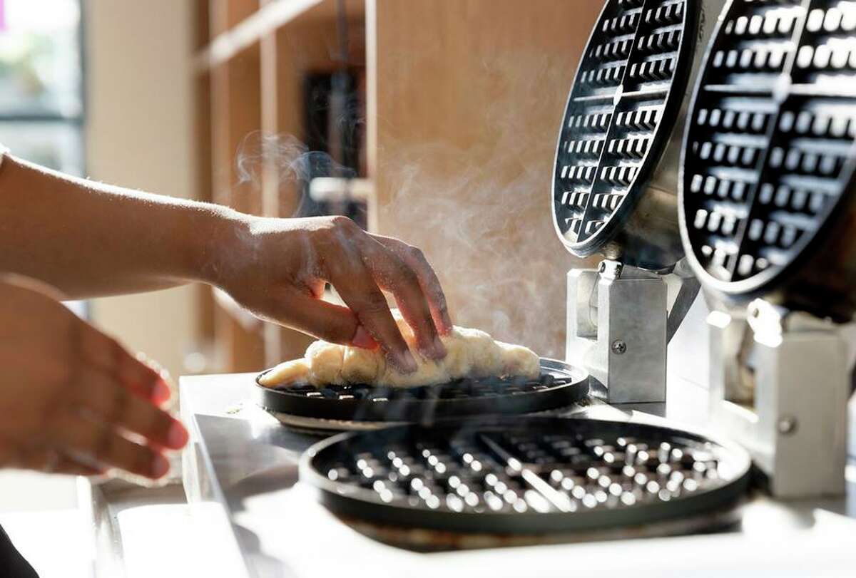 Gaby Lubaba, the founder and head baker at East Bay Bakery, places flattened and sugar-coated croissant dough into a waffle iron as she makes a batch of croffles at her bakery in Danville.