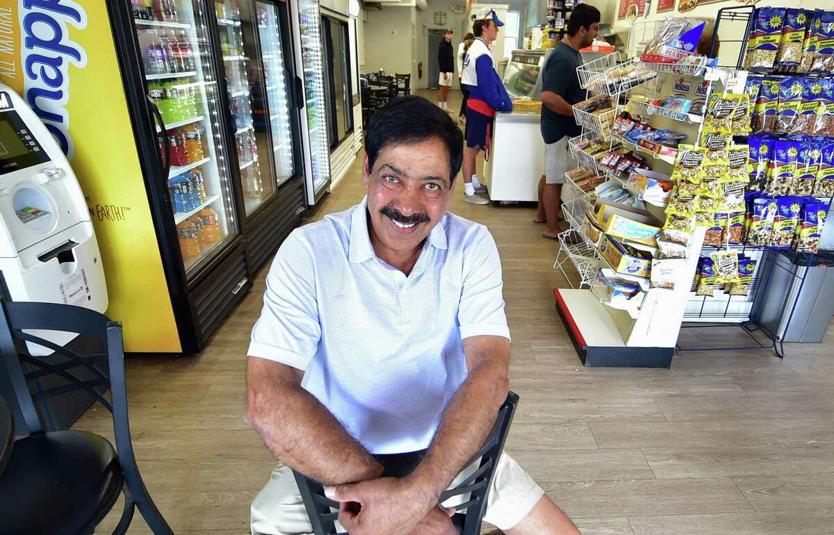 Sam Chidella, at right, poses at Mama Carmela's Deli, where he likes to hang out in Darien, on Tuesday July 26, 2022. Chidella, a manager at Darien Exxon Mobil for 25 years, is retiring and heading back to India, his home country.