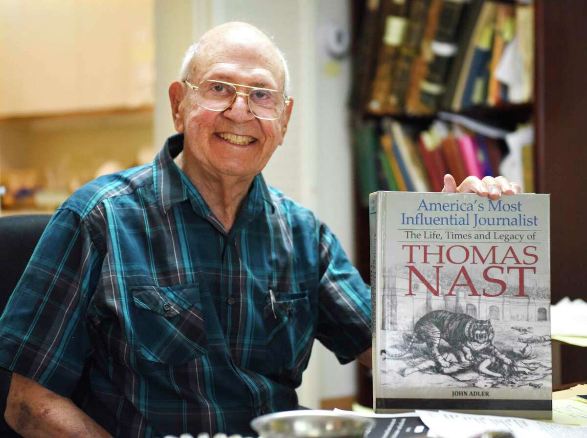 Author John Adler, 94, poses with his new book "America's Most Influential Journalist: The Life, Times and Legacy of Thomas Nast" at his home in the Riverside section of Greenwich, Conn. Monday, Aug. 8, 2022. Adler has a forthcoming book about the life and work of pioneering political cartoonist, Thomas Nast, and owns substantial collection of Nast's work.