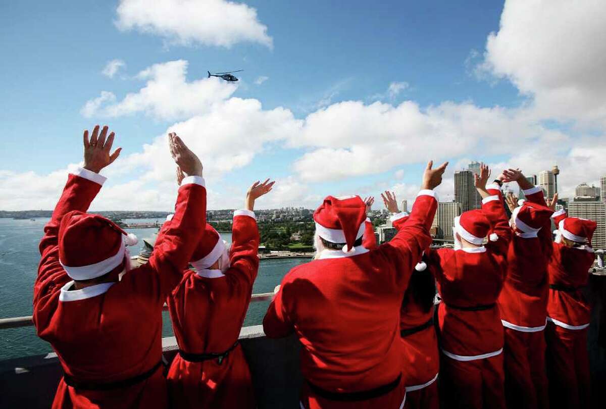SYDNEY, AUSTRALIA - OCTOBER 06: Volunteers dressed as Santa wave at a tv news helicopter as they stand atop the southern pylon of the Sydney Harbour bridge to launch the Variety Santa Fun Run at Sydney Harbour Bridge on October 6, 2010 in Sydney, Australia. The Variety Children's Charity will host the November 28, five kilometre run to raise funds for Australian children with special needs. Organisers hope the race will attract over 14,000 runners to break the world 'Santa Run' record currently held by Portuagal. (Photo by Graham Denholm/Getty Images)