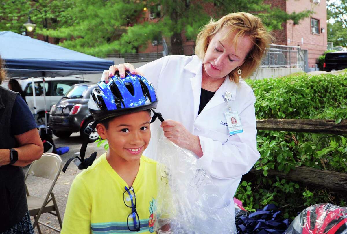 Greenwich Hospital’s Kathy Carley-Spanier fits a bicycle helmet for Angelo Arista during Family Centers Health Care clinic’s annual Community Health Fair.