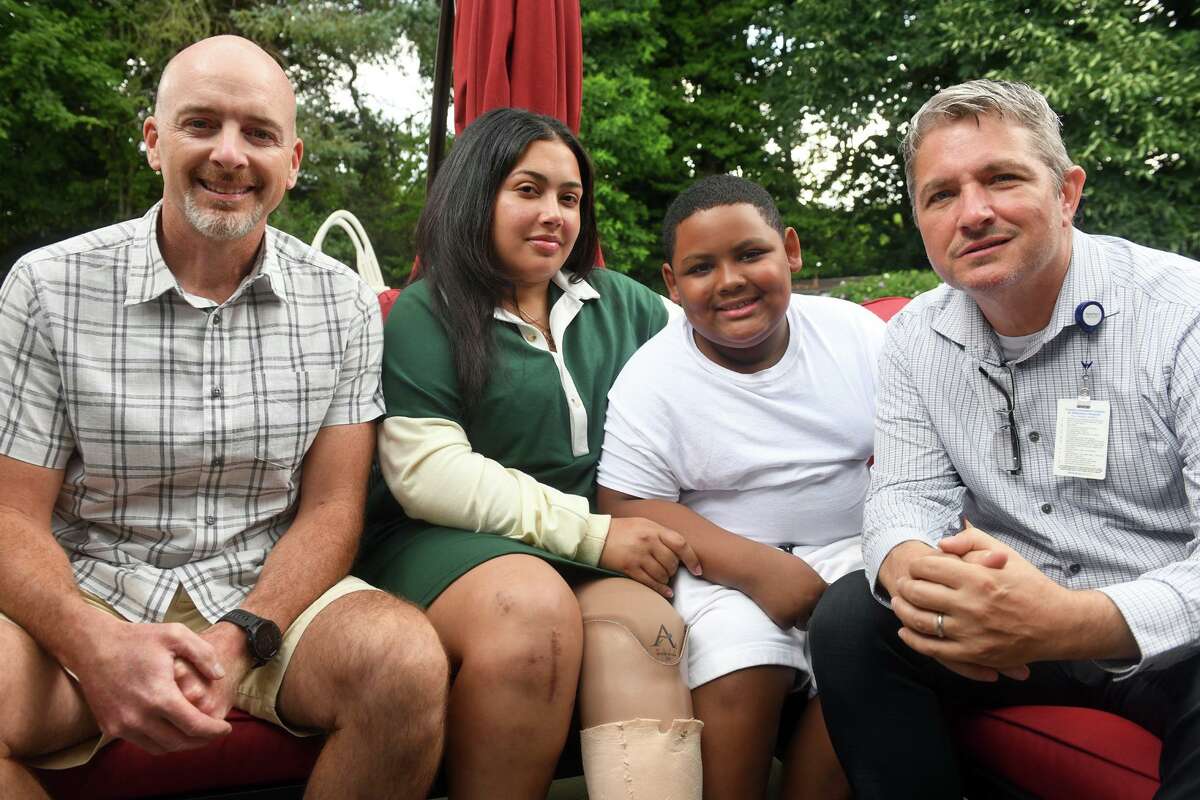 Jailisa Reyes poses with her son, Mark Heyward, and Robert Swercewski, left, and Jeremy Rodrigo, both of Beacon Hose Company No. 1, in Beacon Falls, at Reyes’ home in Bridgeport, Conn. Aug. 9, 2022. Heyward and Swercewski helped save Reyes’ life after her car was hit head on by a wrong way driver on Route 8 in August 2021.