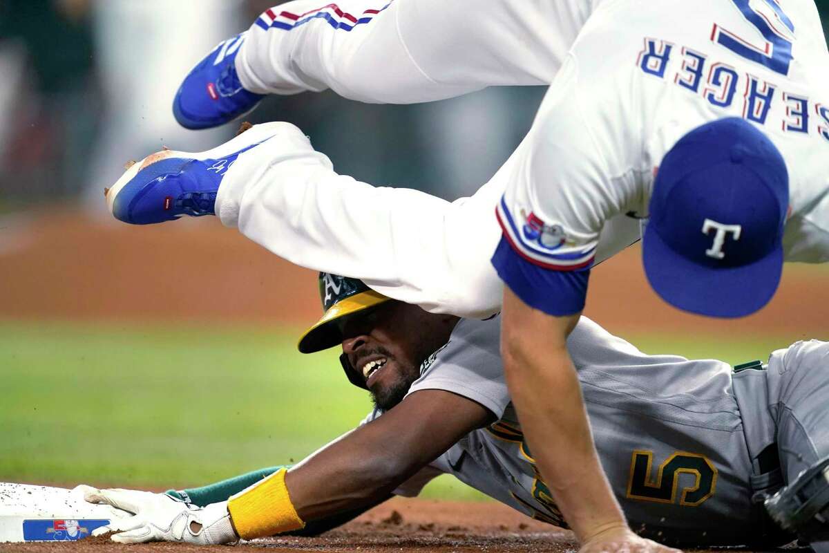 Oakland Athletics' Tony Kemp holds on to third base as Texas Rangers shortstop Corey Seager falls over him while grabbing the throw during the first inning of a baseball game in Arlington, Texas, Tuesday, Aug. 16, 2022. Kemp advanced to third on a single by Seth Brown that also scored Cal Stevenson. (AP Photo/Tony Gutierrez)