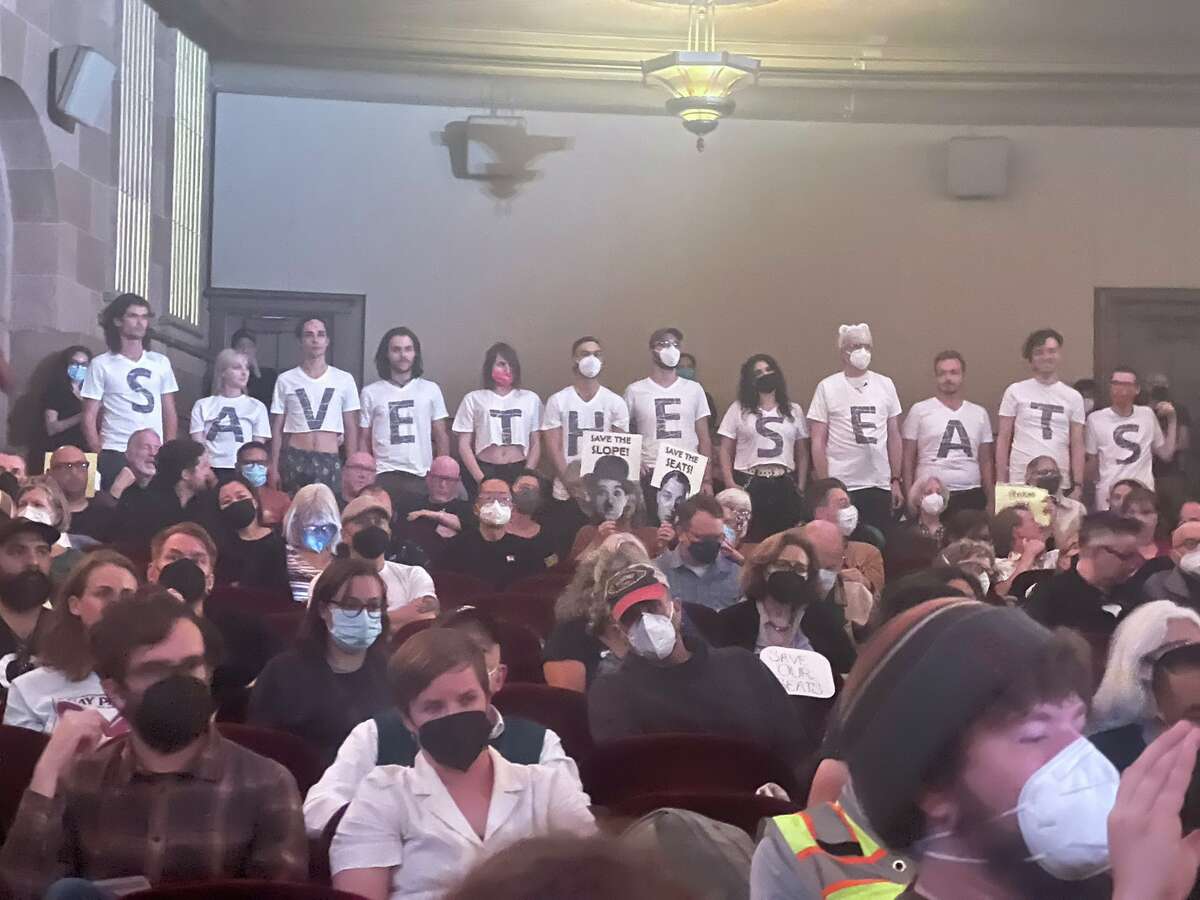 La gente usa camisetas que dicen, "guardar los asientos" 2022 durante el encuentro comunitario realizado en el Teatro Castro. 