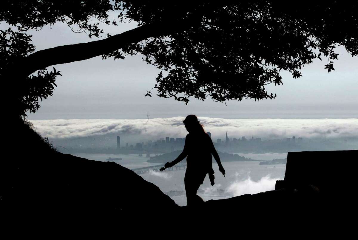 Danielle Roush against the view of fog rolling across the San Francisco skyline and into San Francisco Bay as seen from Grizzly Peak Blvd. in Berkeley, Ca. on Wednesday on April 3, 2013. Rain showers are expected to move across the Bay Area tomorrow morning. Michael Macor, SFChronicle