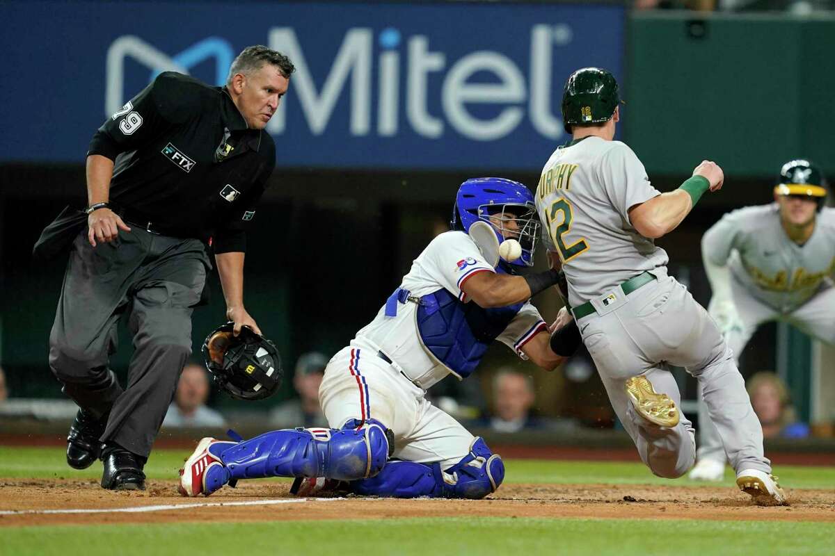 Umpire Manny Gonzalez (79) looks on as Texas Rangers catcher Meibrys Viloria loses the ball while trying to tag out Oakland Athletics' Sean Murphy (12) who scored on a single by Chad Pinder in the eighth inning of a baseball game, Wednesday, Aug. 17, 2022, in Arlington, Texas. (AP Photo/Tony Gutierrez)