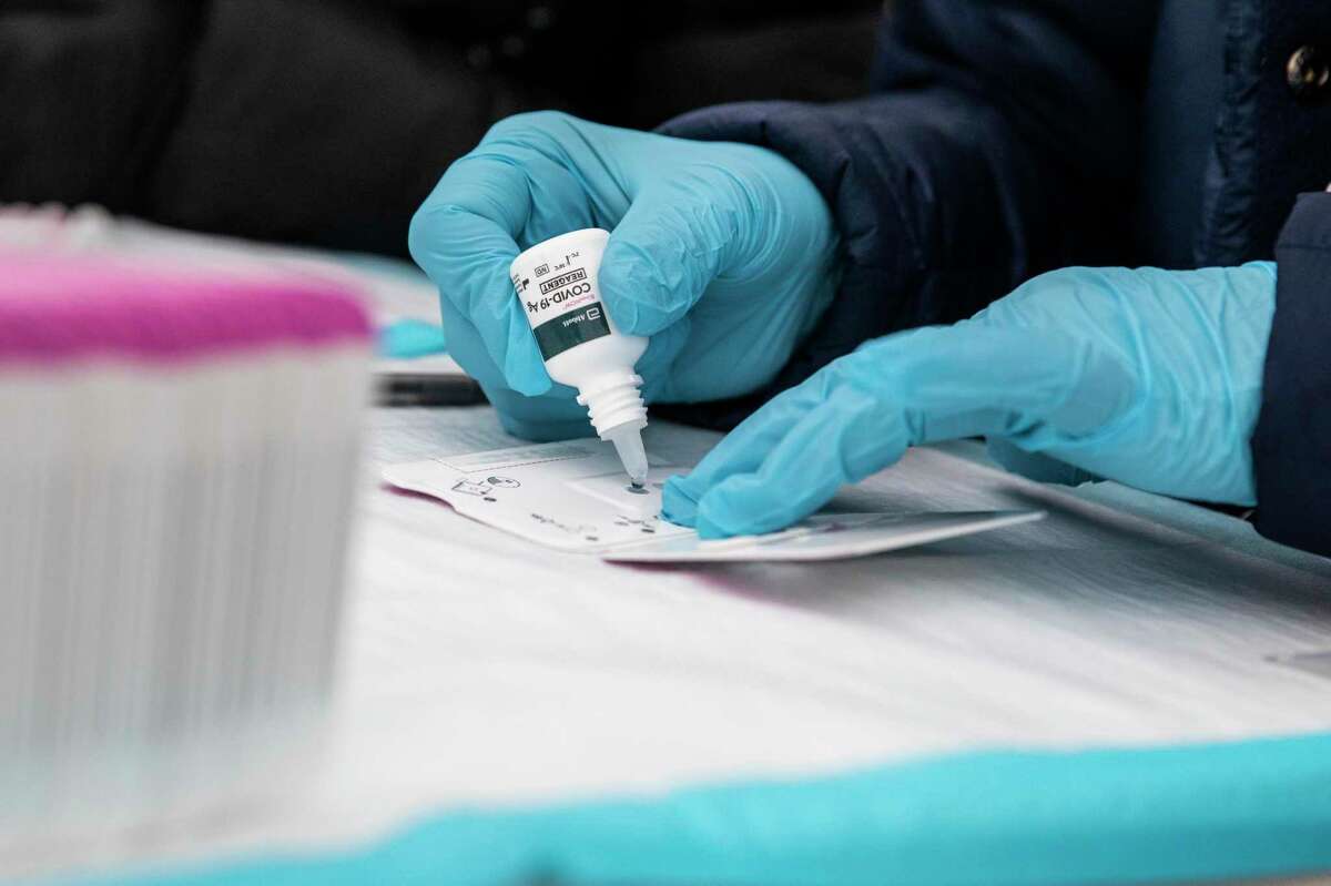 2022年1月，一名抽血师在旧金山的一个社区检测点准备COVID-19快速测试卡。从周一开始，加州将会这样做不再需要口罩在医疗机构中预防COVID-19 -隔离，这是该州以前强制性COVID规则的最后残余。 