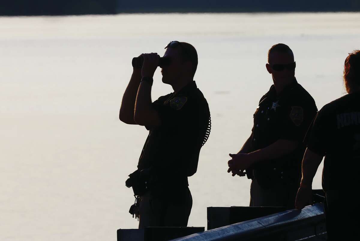 Madison County deputy sheriffs use binoculars to scan the river for a woman who was reported floating in it Thursday evening around 6 p.m.